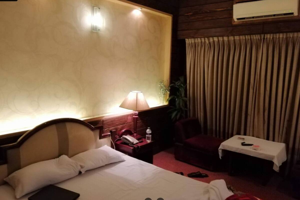 Una habitación de hotel con cama, lámpara de noche, silla, mesa y cortinas.