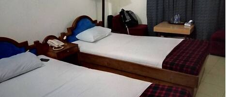 A hotel room with two single beds, a bedside table with a phone, a lamp, and a small table with a water bottle and tissues.