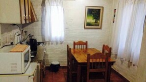 A compact kitchen with a dining table and chairs, a microwave, and a small trash bin.