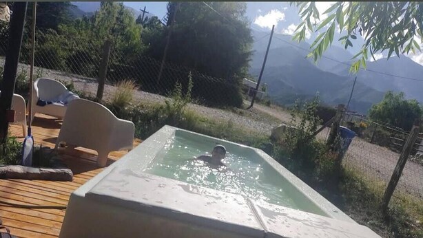 A swimming pool with a person in it, surrounded by a deck with chairs, overlooking a mountainous landscape.