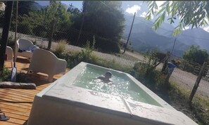 Piscina con una persona, rodeada por una terraza con sillas, con vista a un paisaje montañoso.