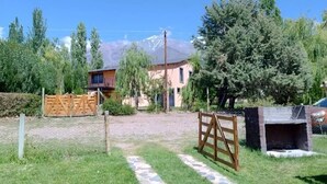 A grassy area with a stone pathway leading to a wooden gate, a dog lying on the grass, and a building in the background.