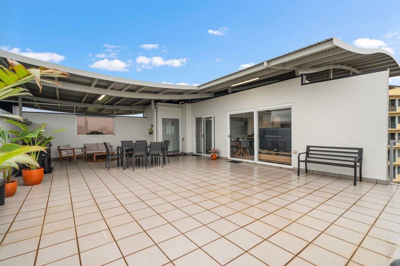 A spacious patio with a dining area, a bench, and potted plants.