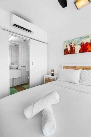 A hotel room with a bed, a nightstand, a painting, and an air conditioning unit. - Zen Bayline Villa: bayview - balcony - rooftop (Darwin City)