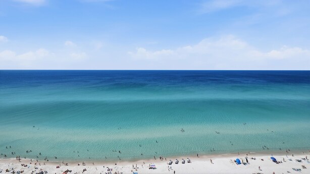 Une plage à l’eau turquoise et limpide, un rivage sablonneux et un ciel dégagé.