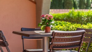 Una mesa en el patio con una planta en maceta, una silla y vistas de un jardín cuidado.