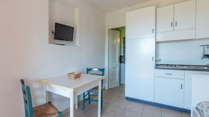 Habitació petita i senzilla amb taula i cadires, televisió penjada a la paret i una cuineta amb armaris i fogó.
