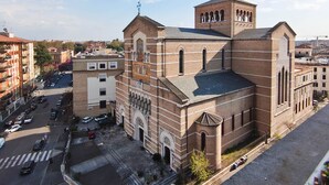 Un grand bâtiment en briques, doté d’un imposant clocher et de fenêtres en arc de cercle, situé dans un quartier urbain, entouré d’autres bâtiments et bordé par une rue.
