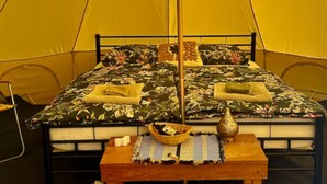 Ein Zelt mit Bett, Kissen, einem Tisch mit einer Vase und einem Korb.