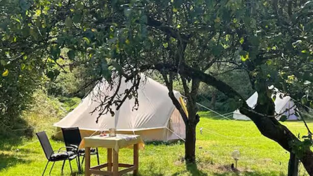 Ein Zelt auf einer Wiese, in der Nähe ein Tisch und Stühle.