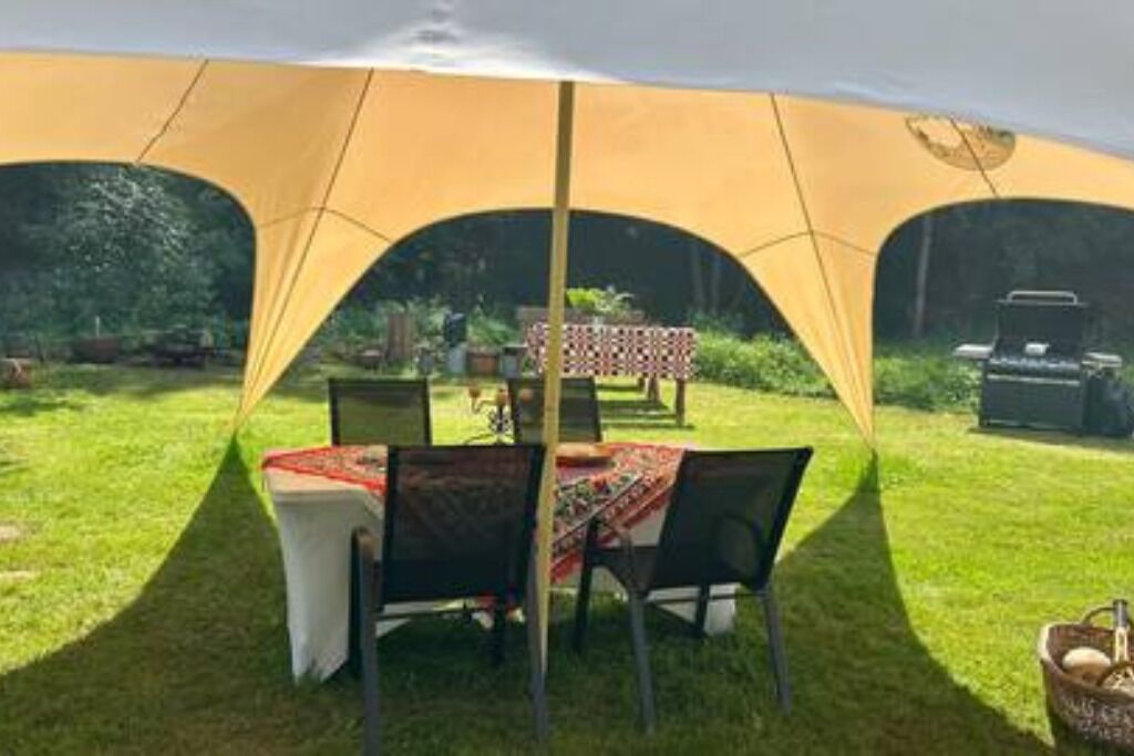 Ein Zelt mit Tisch und Stühlen im Freien, umgeben von Gras und Bäumen.