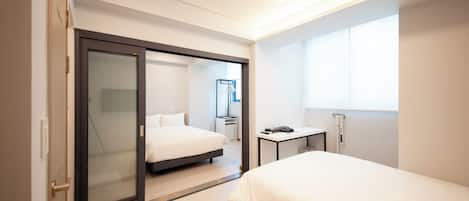 A modern hotel room with a bed, a desk, a mirror, and a sliding door.