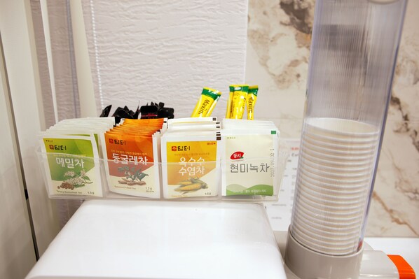 Una estación de té con diferentes paquetes de té y una pila de vasos desechables.