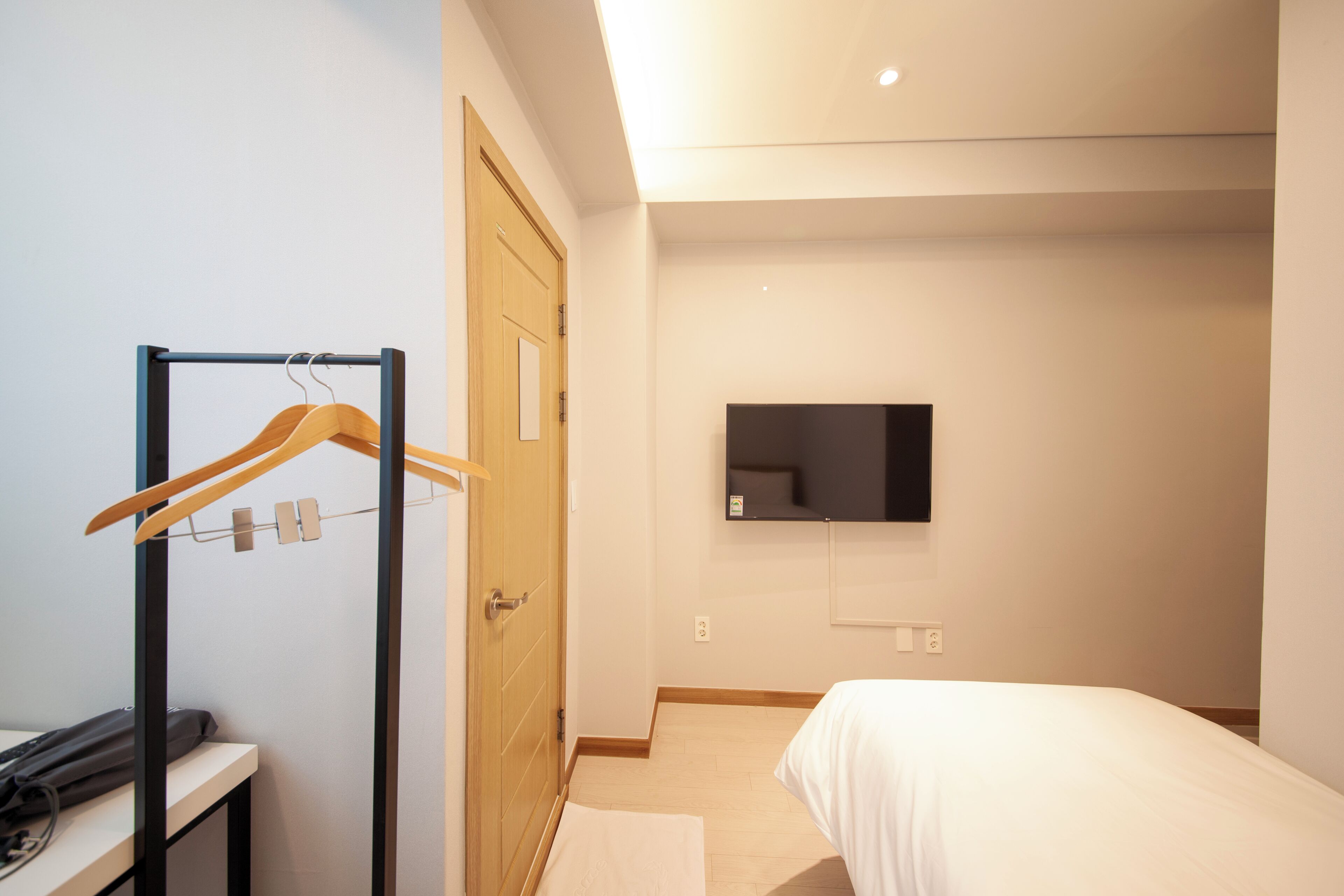 Un dormitorio con una cama, una puerta de madera, un espejo y un televisor de pared.