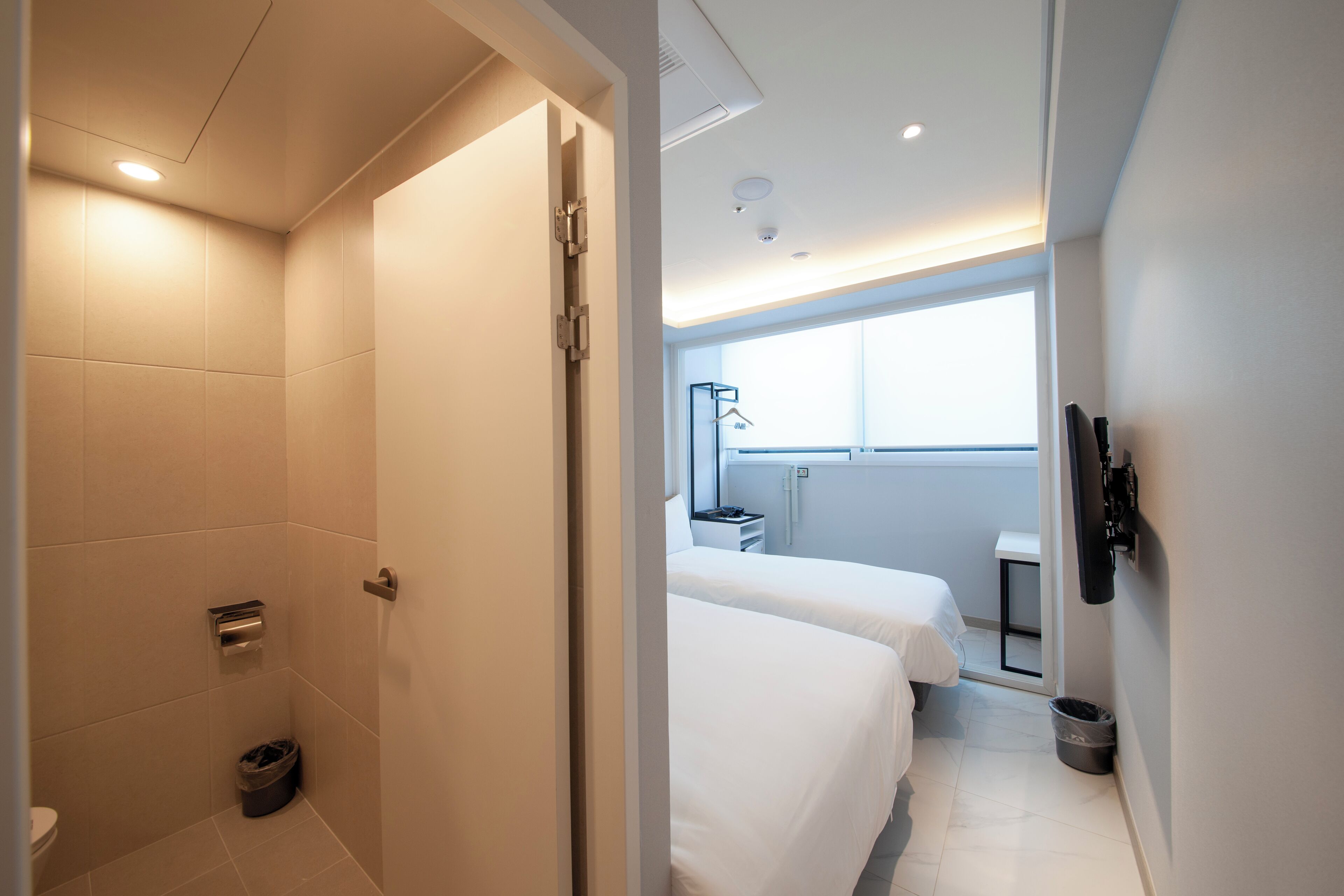 A modern hotel room with a shower, a bed, a small table, and a window.