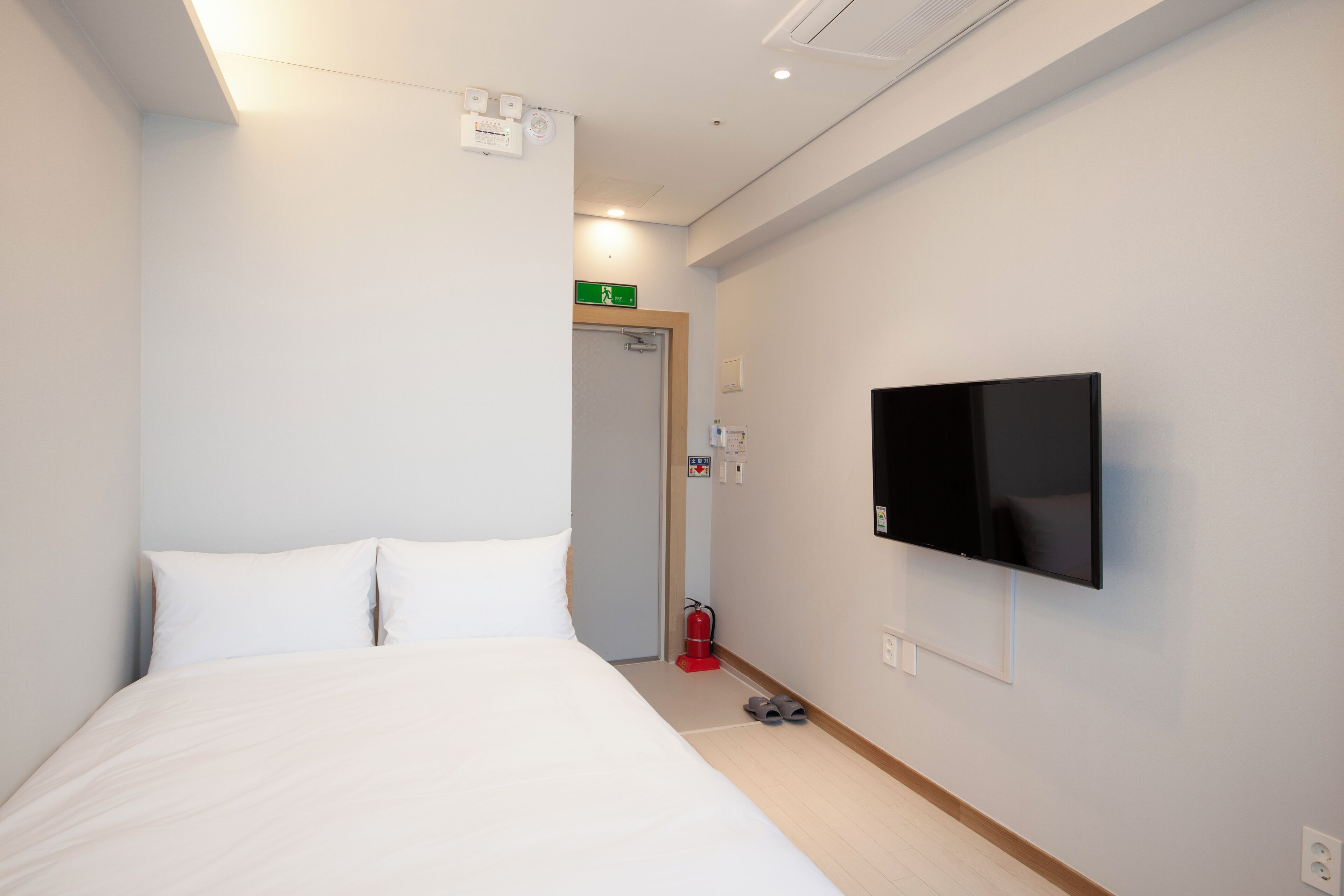Une chambre d’hôtel équipée d’un lit, d’un téléviseur à écran plat fixé au mur, d’un extincteur et d’un panneau d’indication des issues de secours.