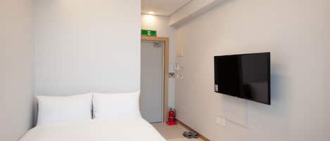Une chambre d’hôtel équipée d’un lit, d’un téléviseur à écran plat fixé au mur, d’un extincteur et d’un panneau d’indication des issues de secours.