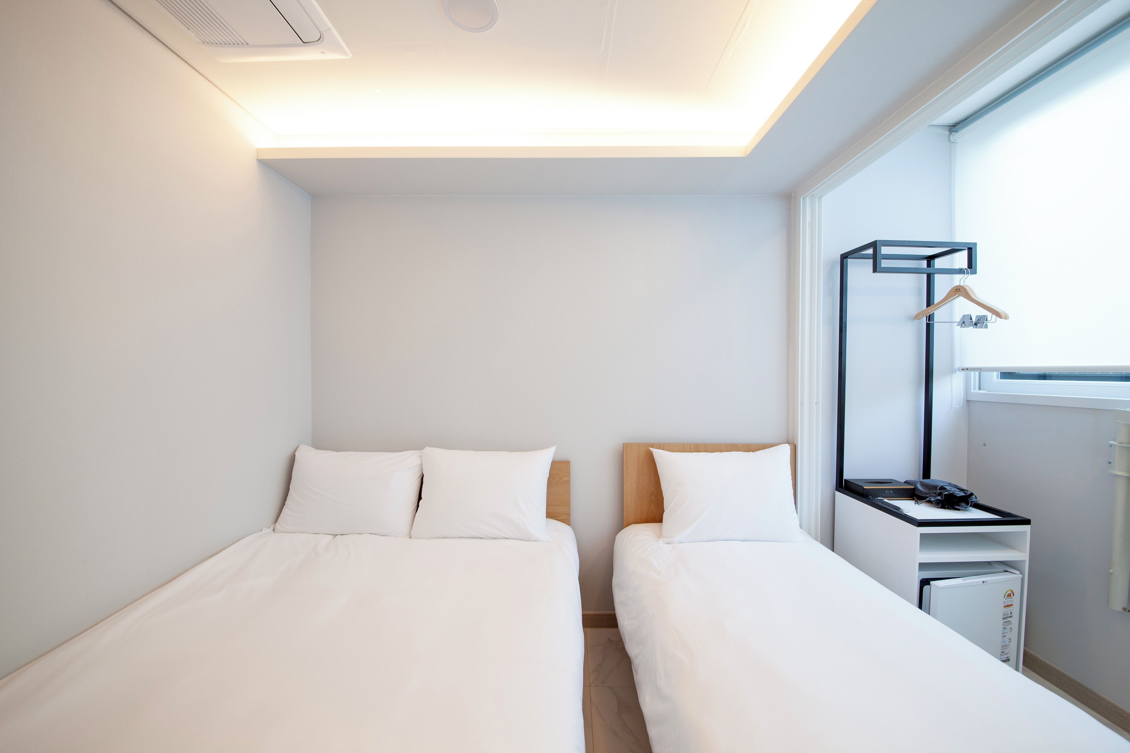 A hotel room with two beds, a desk, a chair, a hanging coat rack, and a window.