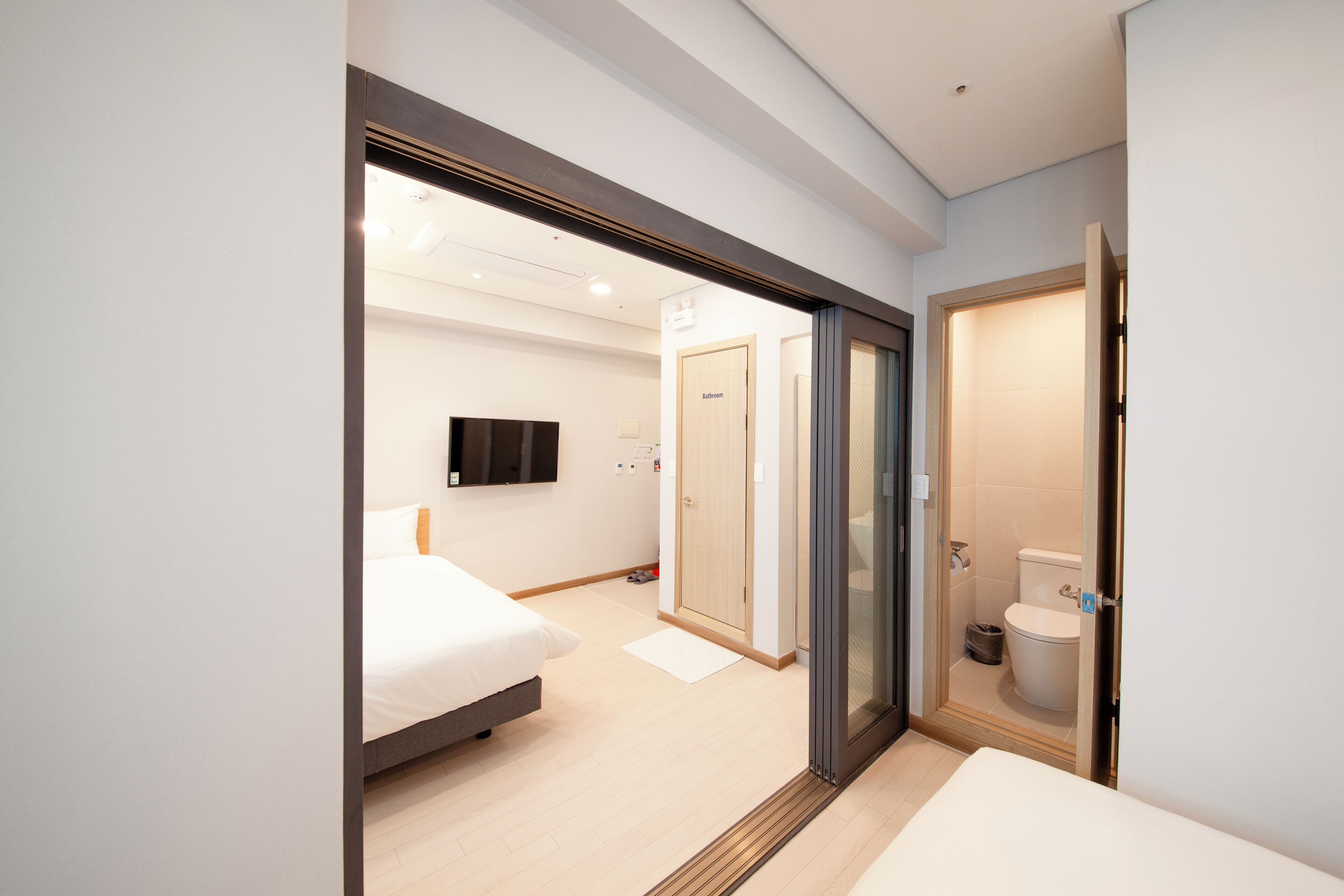 Ein modernes Hotelzimmer mit Bett, Fernseher, Bad mit Toilette und Dusche sowie einer Tür zu einem weiteren Raum.