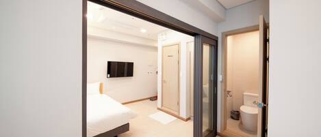 Ein modernes Hotelzimmer mit Bett, Fernseher, Bad mit Toilette und Dusche sowie einer Tür zu einem weiteren Raum.