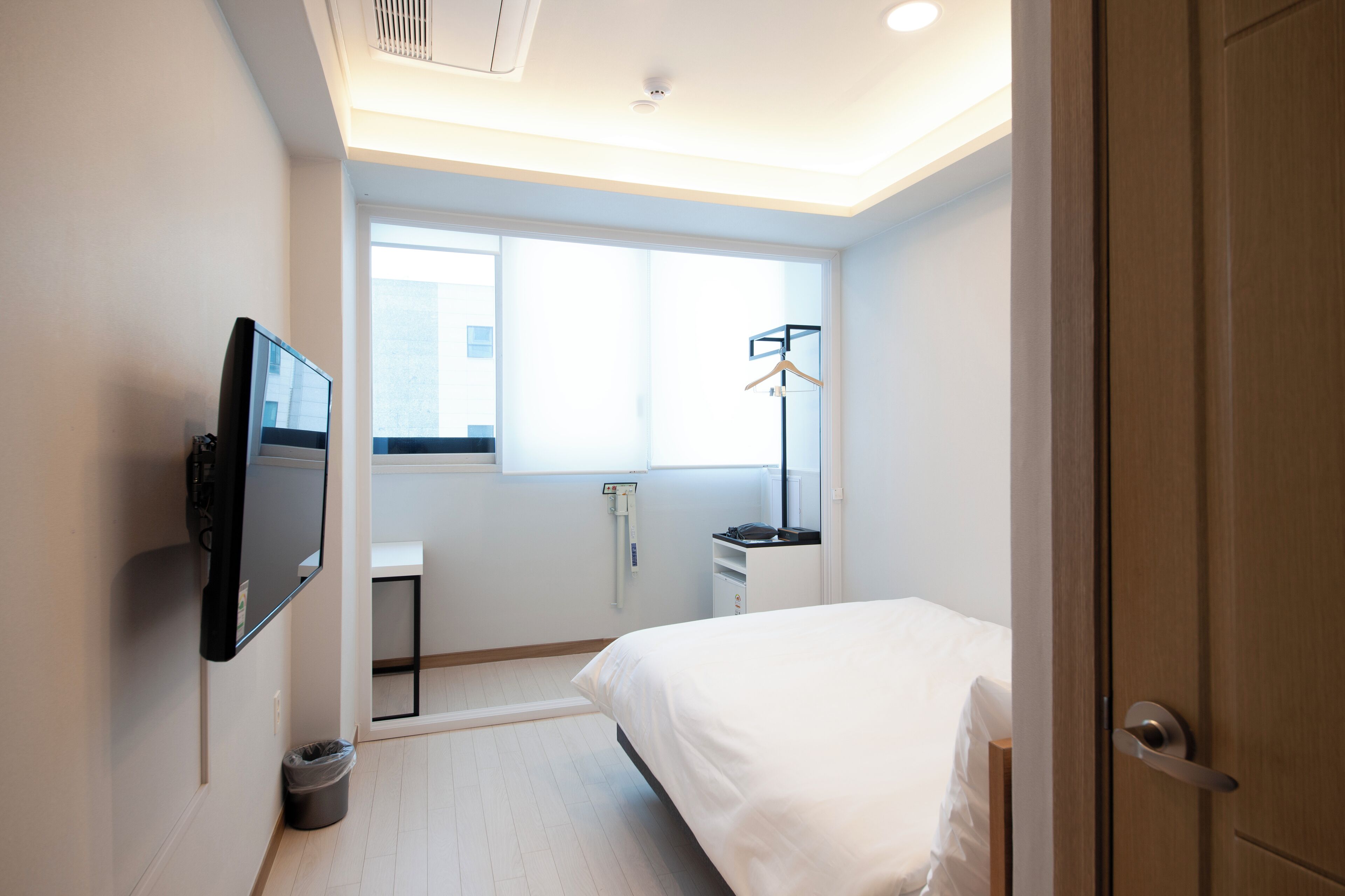 A hotel room with a bed, a TV mounted on the wall, a window, a radiator, and a door.