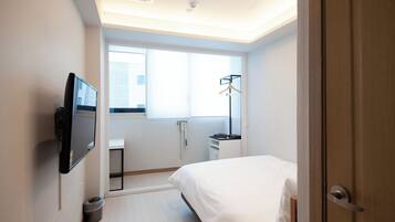 A hotel room with a bed, a TV mounted on the wall, a window, a radiator, and a door.
