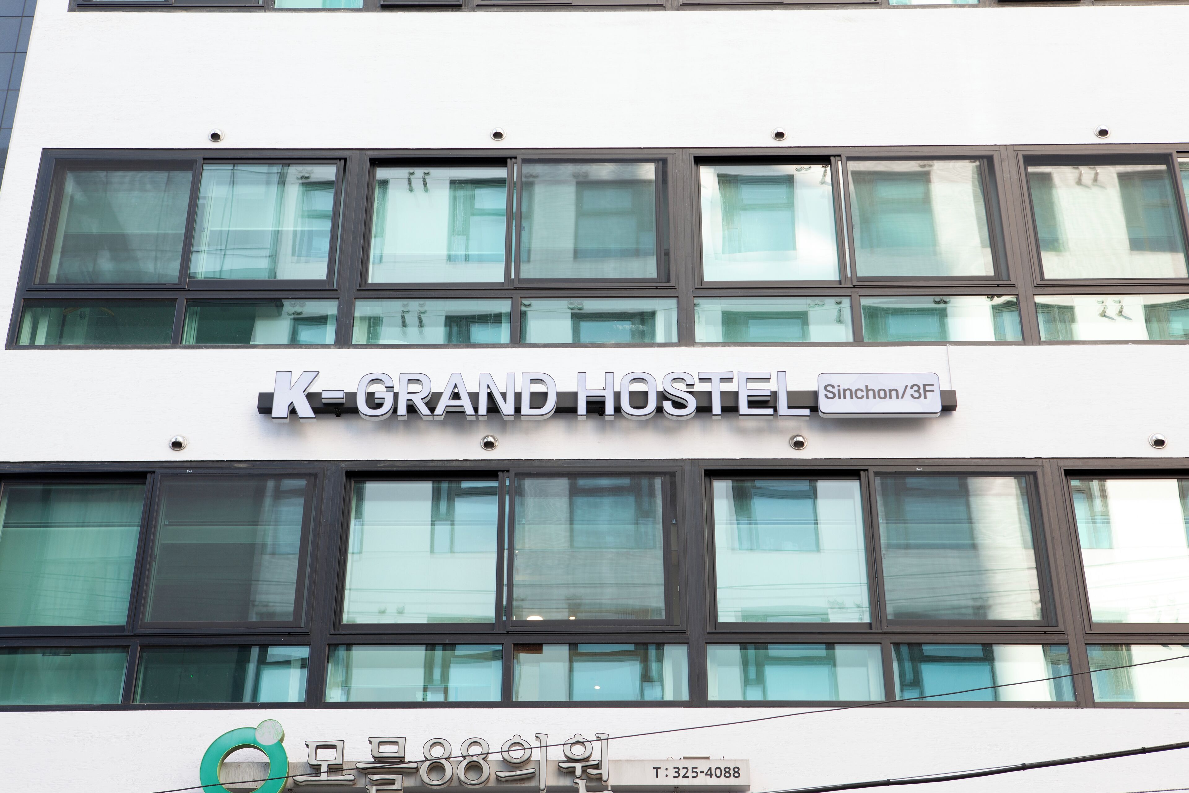 A building with a sign reading 'K-GRAND HOSTEL' and a contact number.