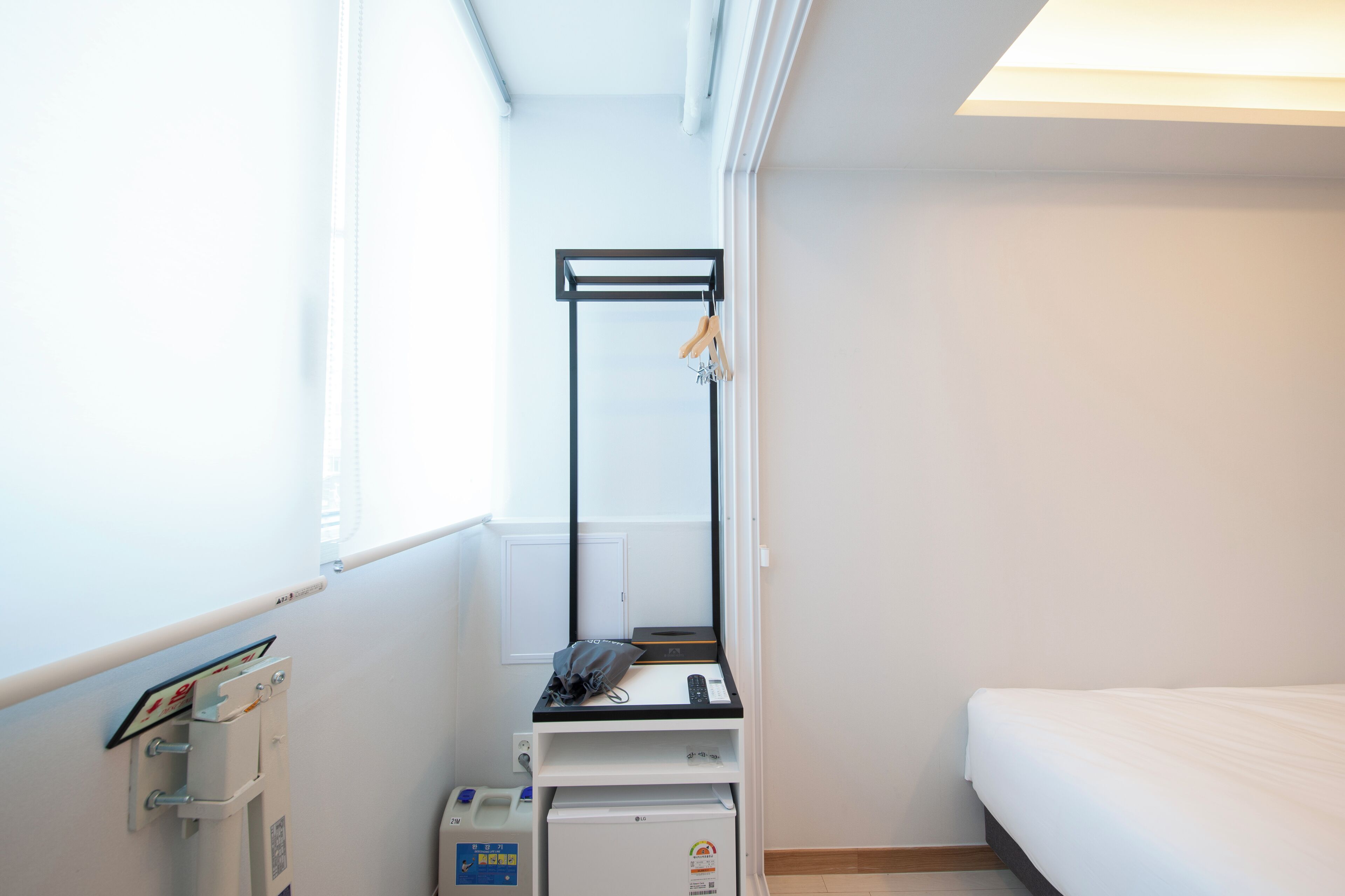 A small, clean room with a bed, a desk with a computer, and a window.