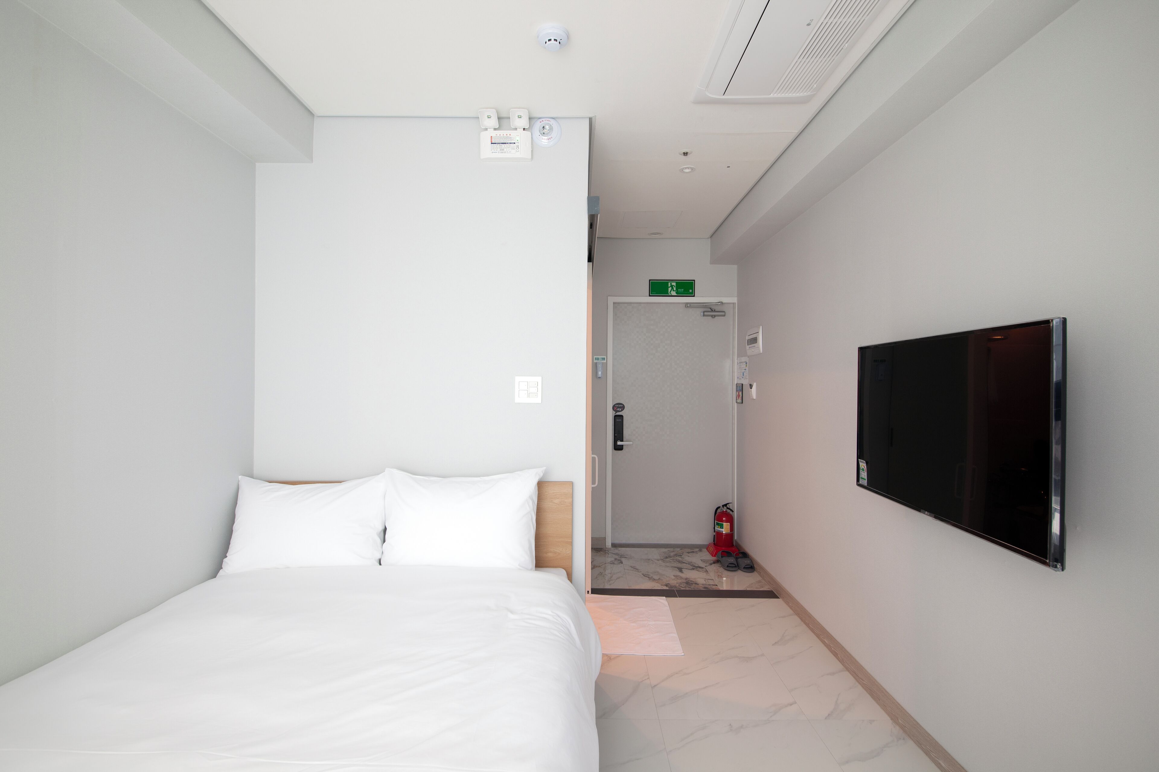 Una habitación de hotel con una cama, un televisor, una puerta que da a un baño y un extintor.