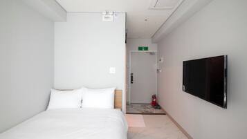 Una habitación de hotel con una cama, un televisor, una puerta que da a un baño y un extintor.