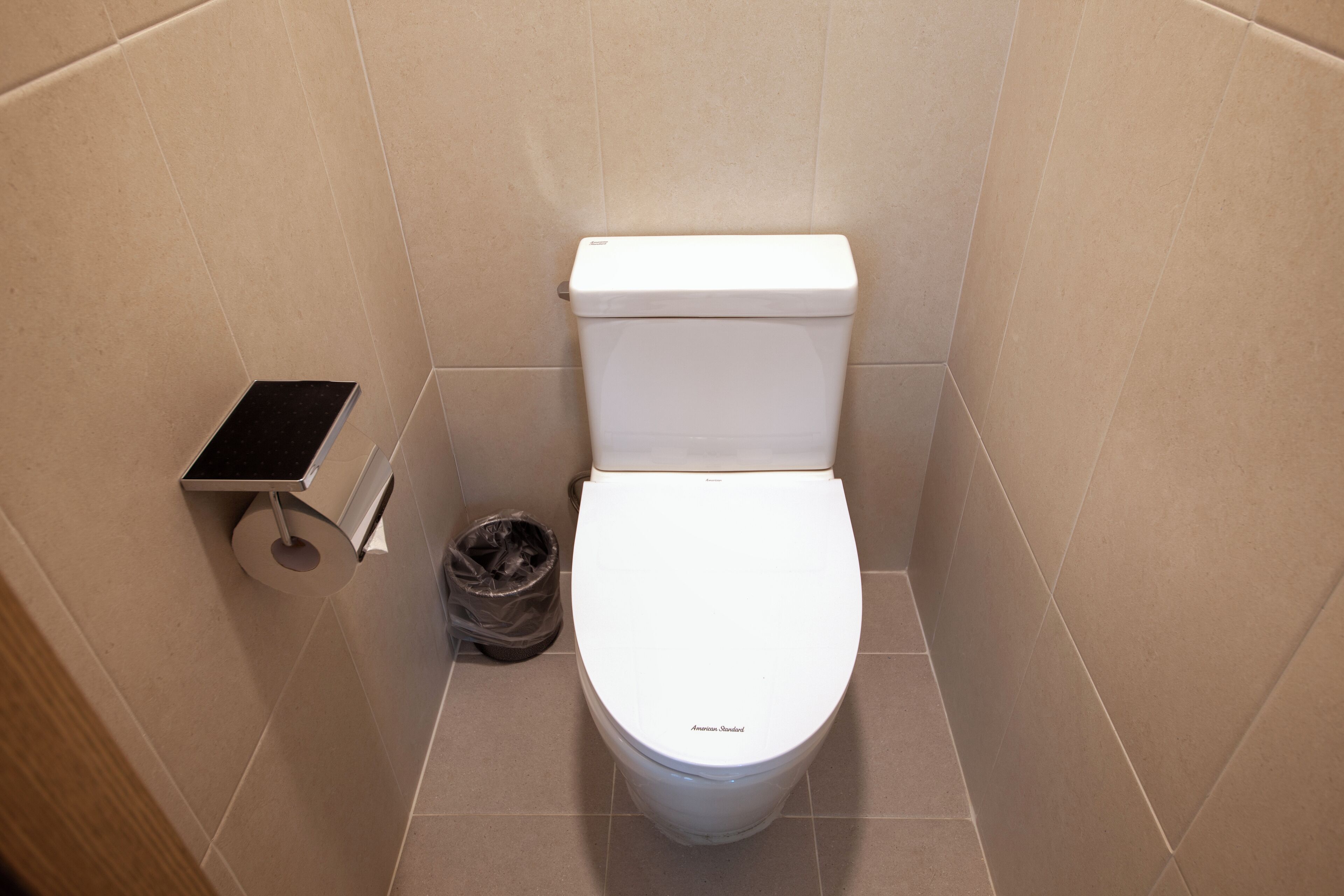 A standard white toilet with a flush handle, a small trash bin, and a toilet paper holder on the wall.