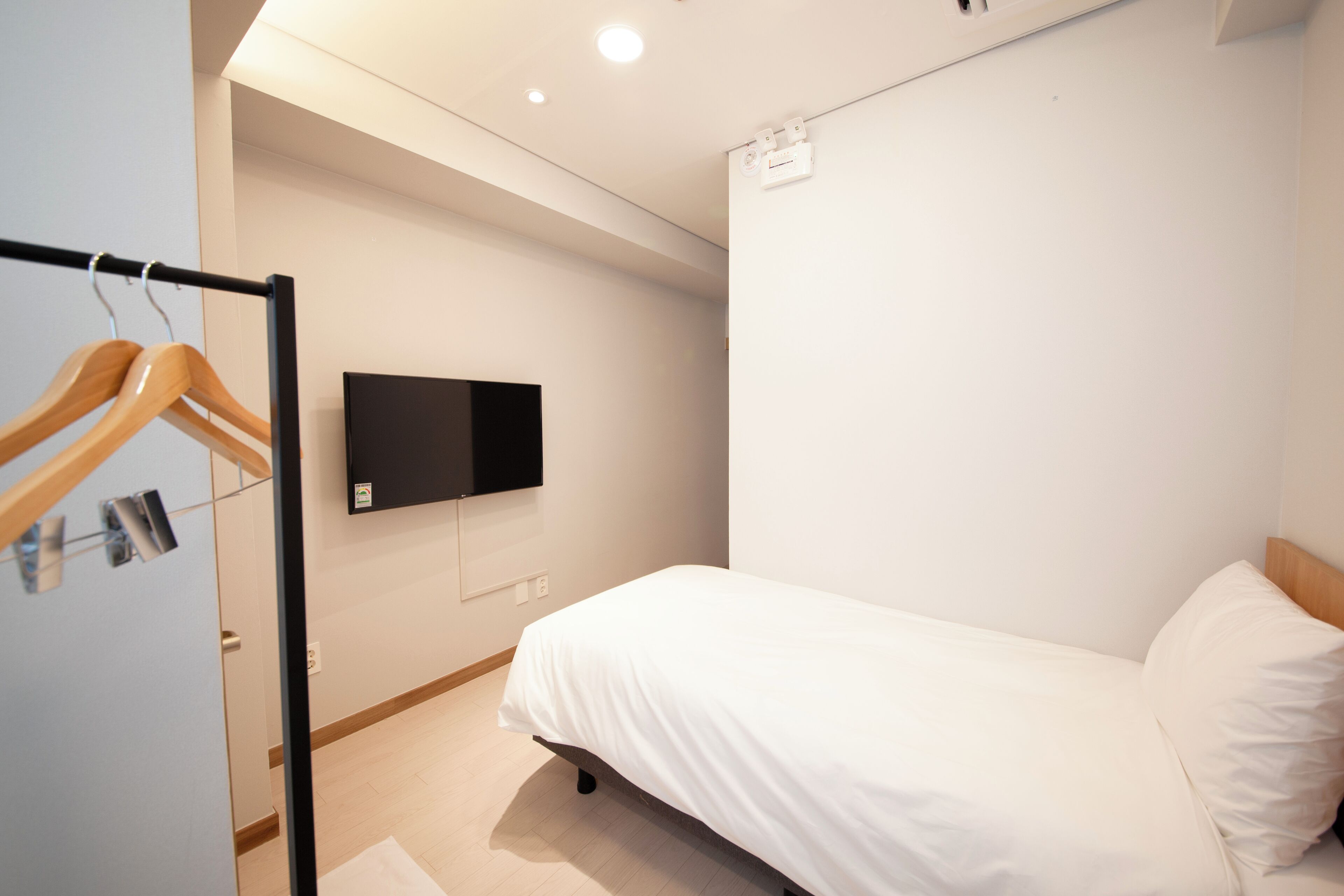 Een slaapkamer met een bed, een aan de muur bevestigde televisie en een houten kledingrek.