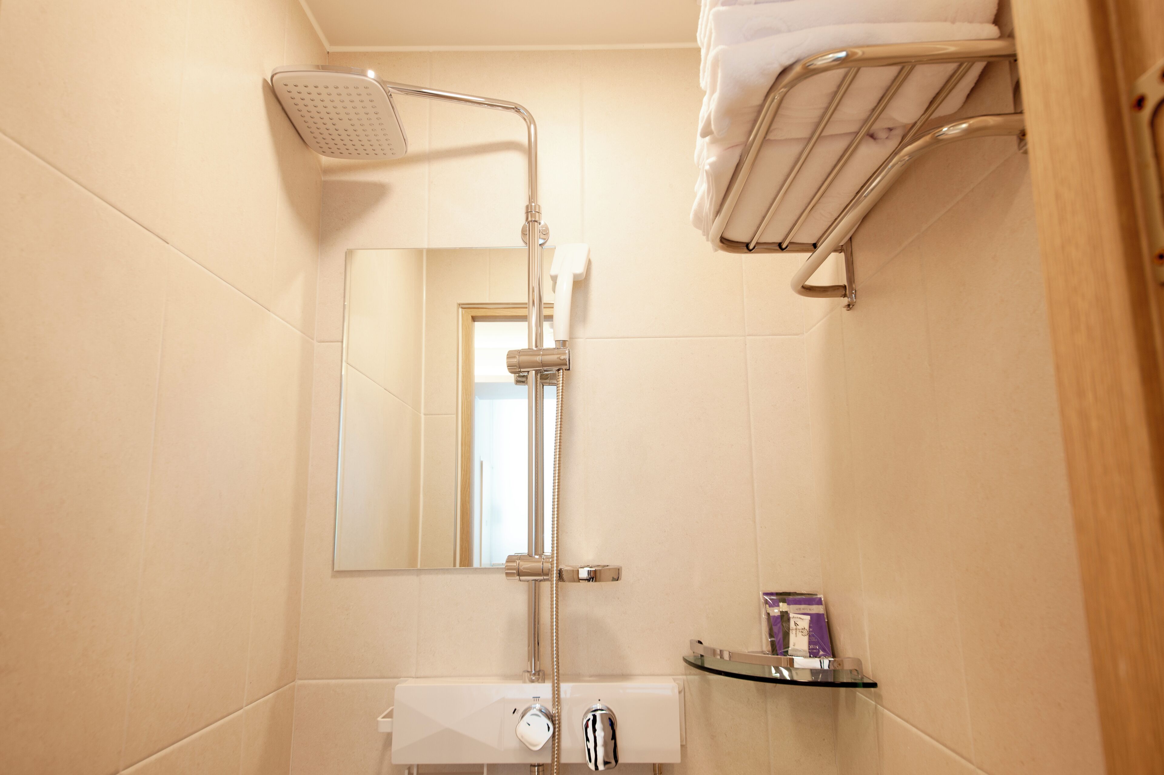 A bathroom with a shower, a mirror, a towel rack, and a small shelf with toiletries.