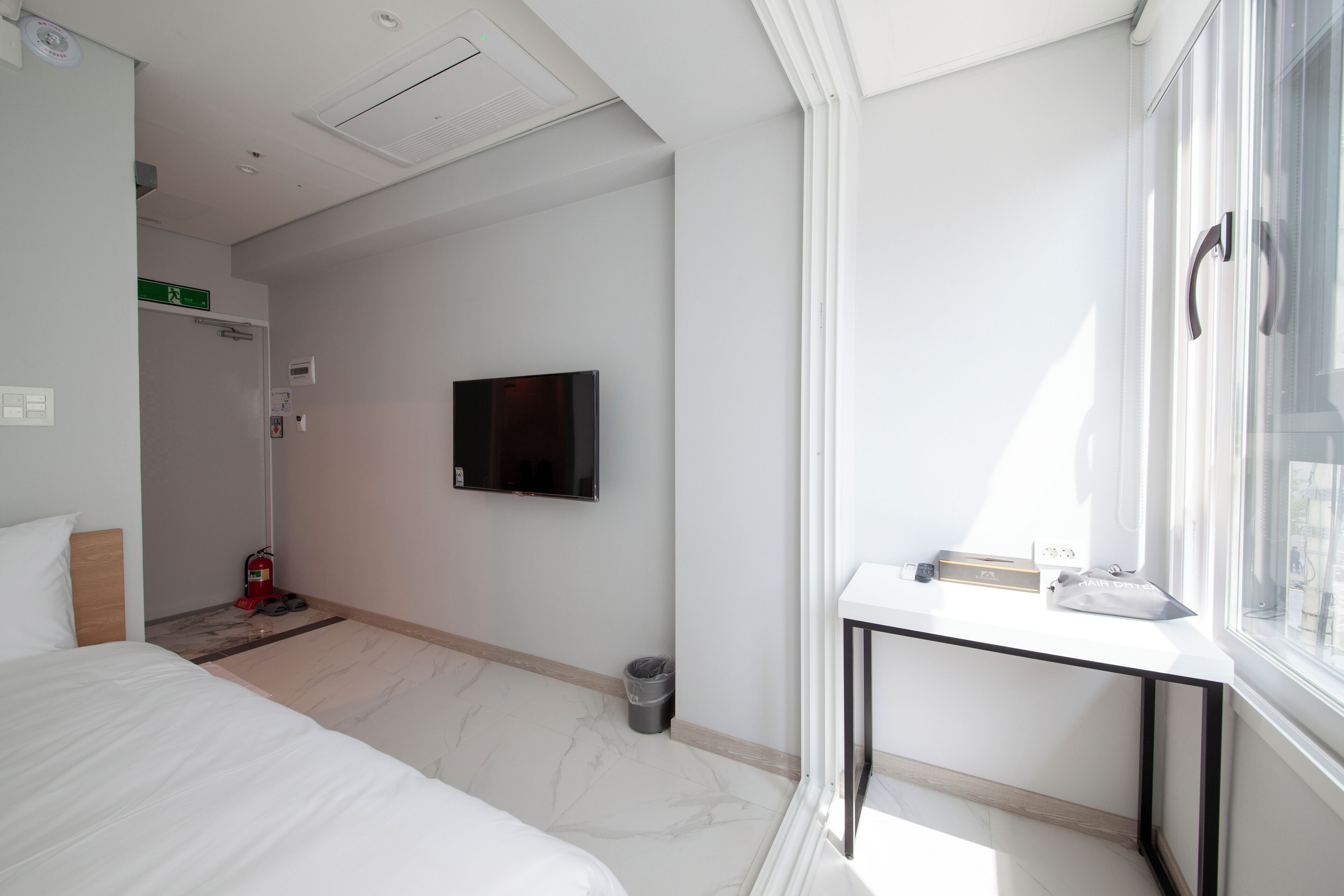 Une chambre d’hôtel avec un lit, un téléviseur fixé au mur, une petite table et une fenêtre.