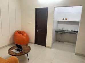 Un espacio habitable compacto con kitchenette, una laptop sobre una mesita y un sillón de peluche.