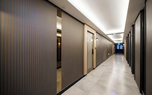 A hotel corridor with doors, a tiled floor, and a ceiling with recessed lighting.