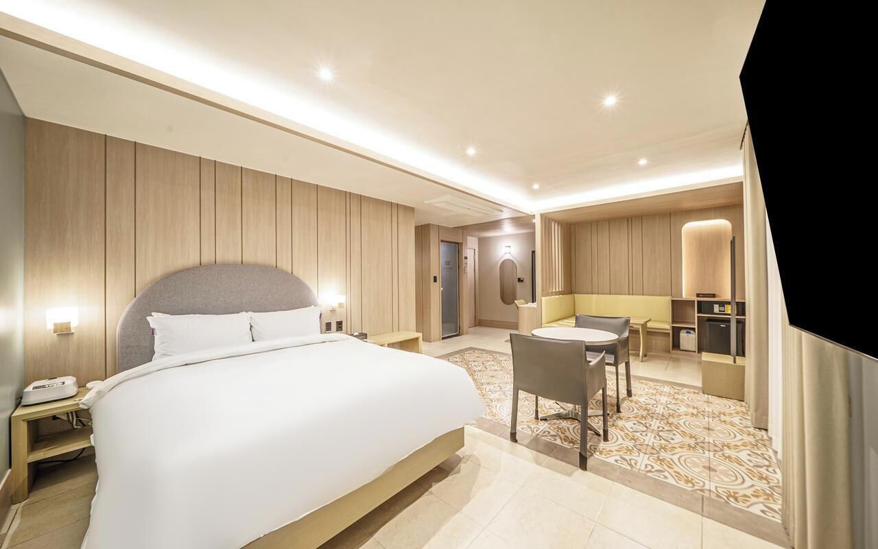 A hotel room with a large bed, a desk, a chair, and a small kitchenette.