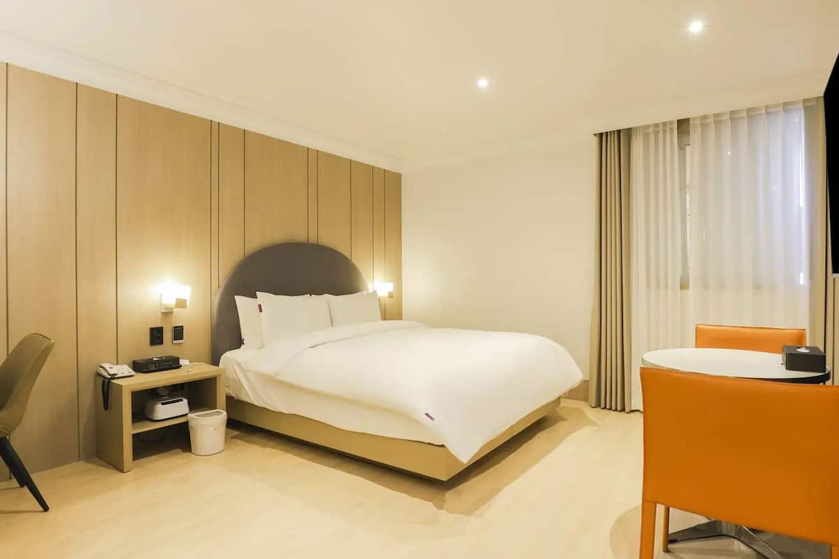 Habitación de hotel con cama, mesita de noche, silla, televisor y cortinas.