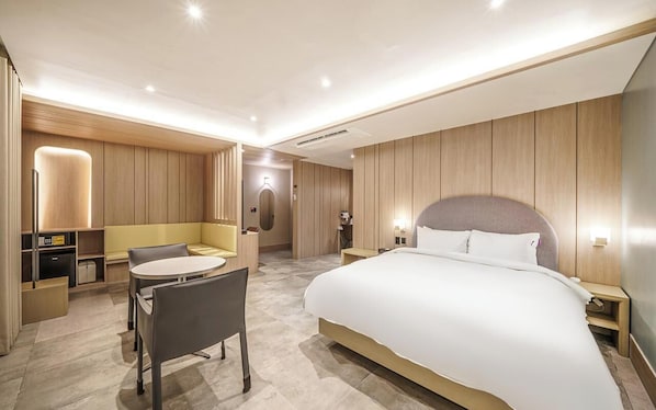 A modern hotel room with a large bed, a seating area with a table, and a separate workspace.