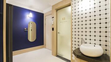 A hotel room with a blue wall, a door labeled 'H. Avenue Hotel,' and a bathroom with a white sink and hexagonal tile backsplash.