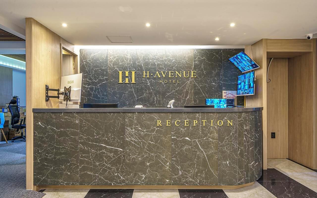 Una recepción con detalles de mármol, el nombre del hotel y una pantalla digital.