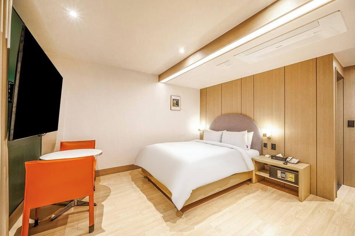 Habitación de hotel con una cama, una mesita de noche con un teléfono, una pequeña mesa con una silla y un televisor montado en la pared.