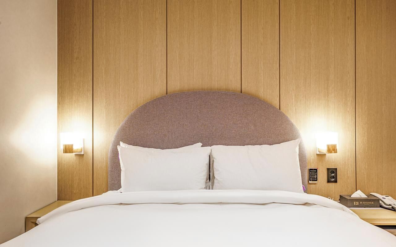 A hotel room with a wooden headboard, a bed with white bedding, two bedside lamps, and a nightstand with a phone and a book.
