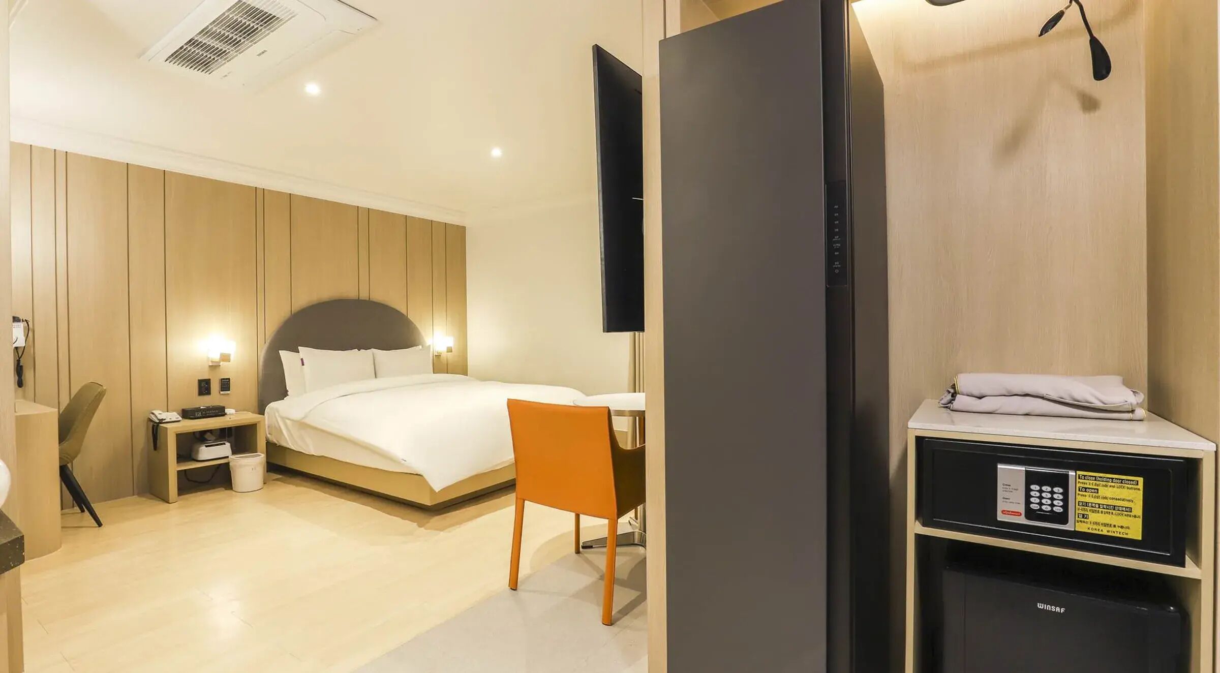 Een hotelkamer met een bed, een bureau, een stoel, een televisie, een verwarming en een bedieningspaneel.