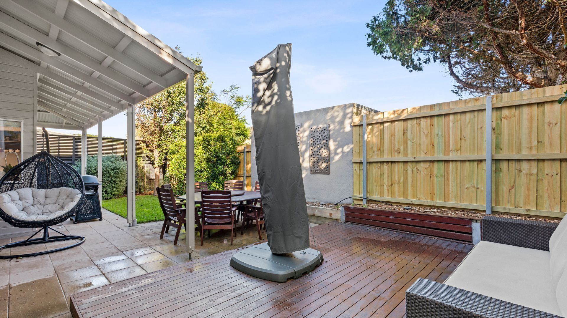 A covered patio with a table and chairs, a hanging chair, and a tall, narrow sculpture.