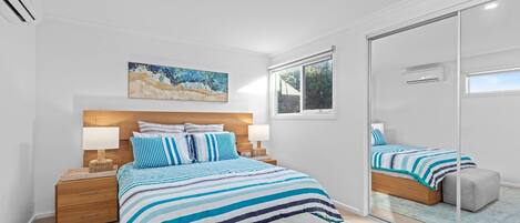 A bedroom with a bed, bedside tables, a nightstand, a mirror, and a window.