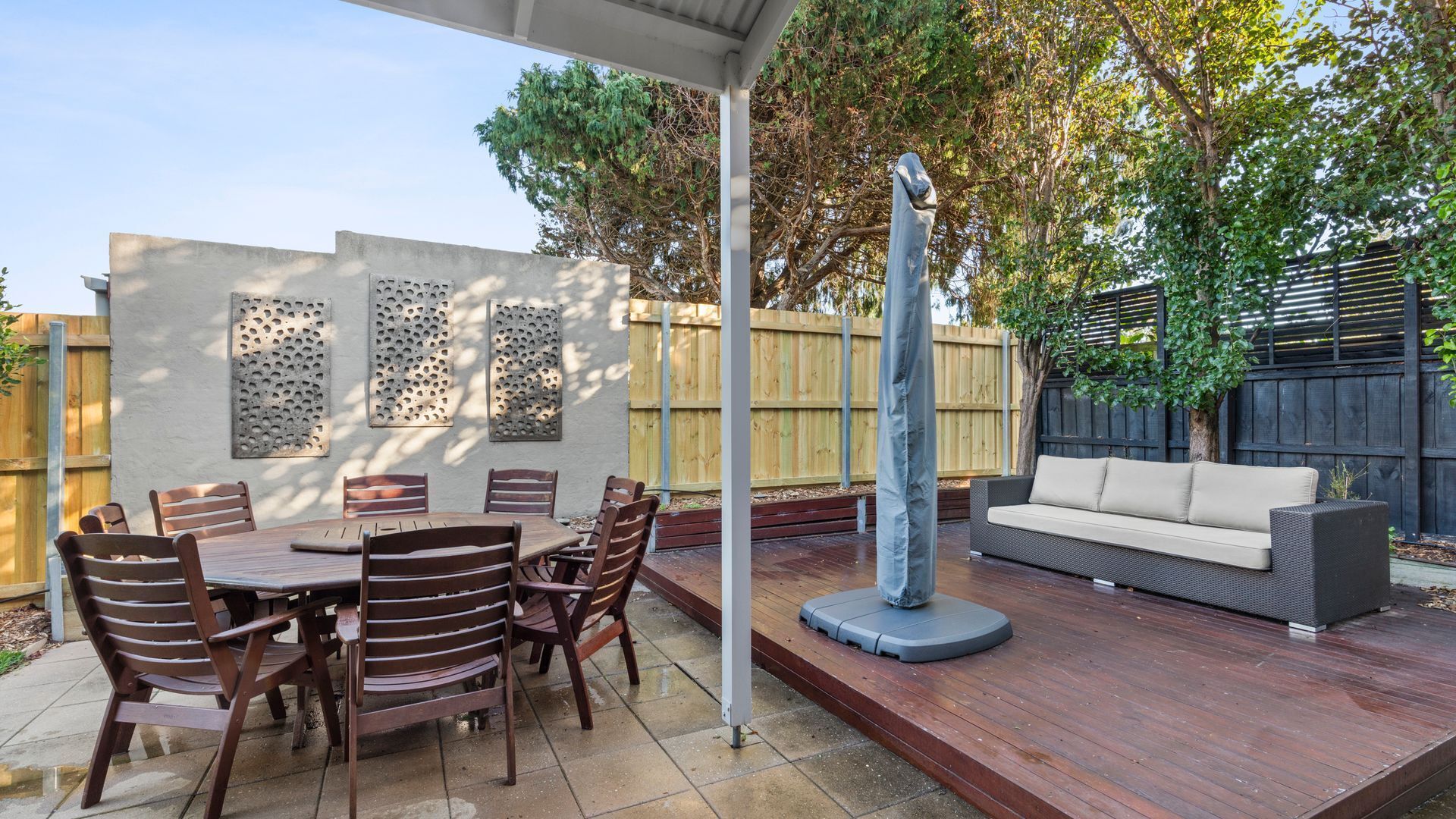 Une terrasse extérieure avec une table ronde et des chaises, un canapé et des panneaux décoratifs sur les murs.