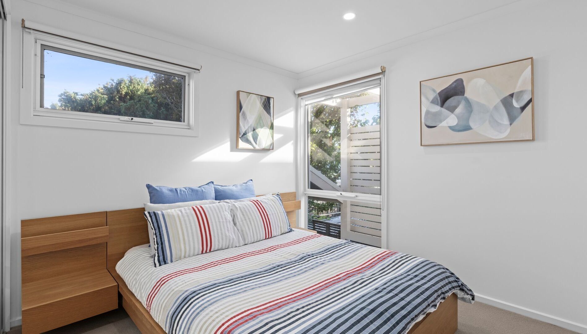 A bedroom with a bed, a window, and two wall-mounted artworks.