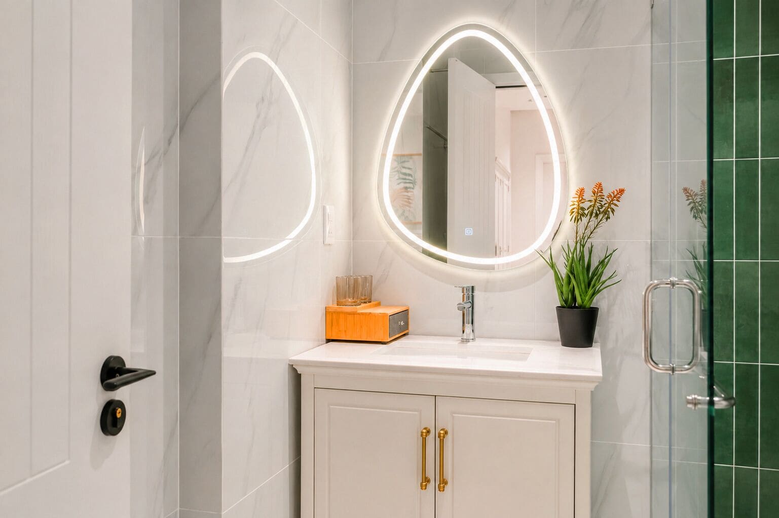 Et badeværelse med en marmorvask, et rundt spejl med LED-lys, en potteplante og et brusekabine i glas.