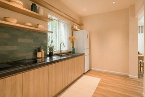 A modern kitchen with wooden cabinets, a black countertop, a built-in stove, and a window with blinds. - Amana Boutique Hotel - Tran Quoc Thao (Ho Chi Minh City)